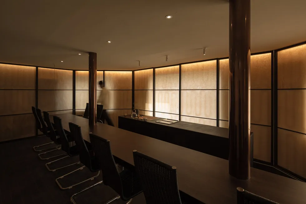A modern industrial-style office board room with wooden tables and chairs, large windows, and copper columns.