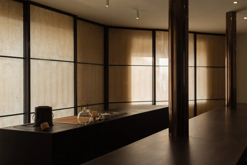 A minimalist tearoom with wooden flooring, a wooden bench, and a glass teapot on a wooden surface.