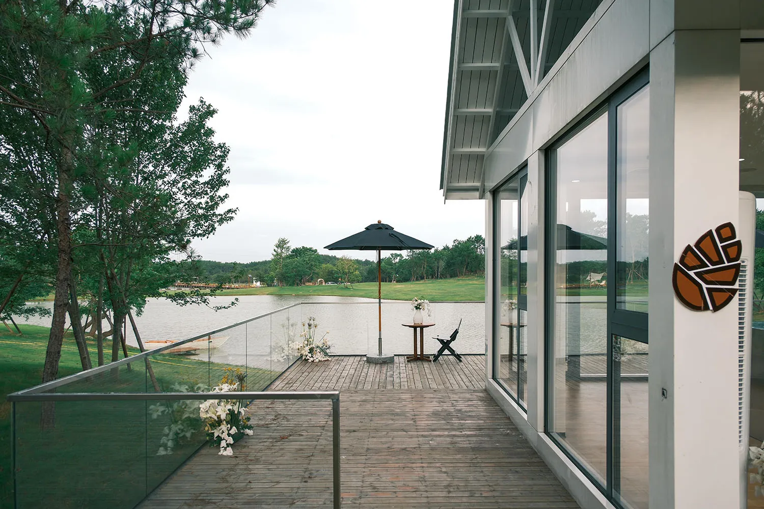 Wooden deck with glass railing overlooking a serene water body. Modern furniture and decorative elements.