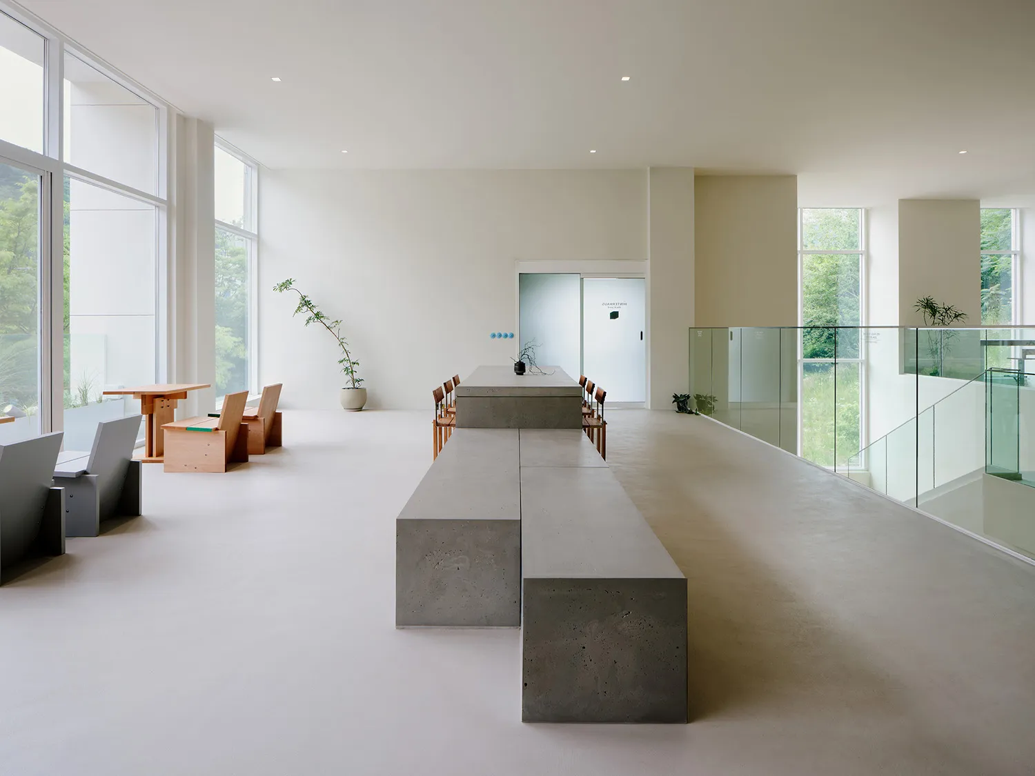 A modern minimalist office space featuring a concrete floor and a glass wall overlooking the greenery.