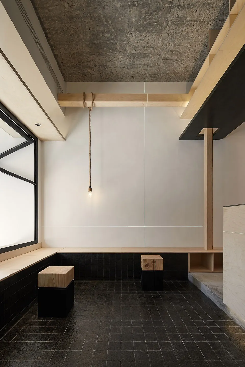 A minimalist living space featuring a concrete wall, black tiled floor, and wooden furniture.