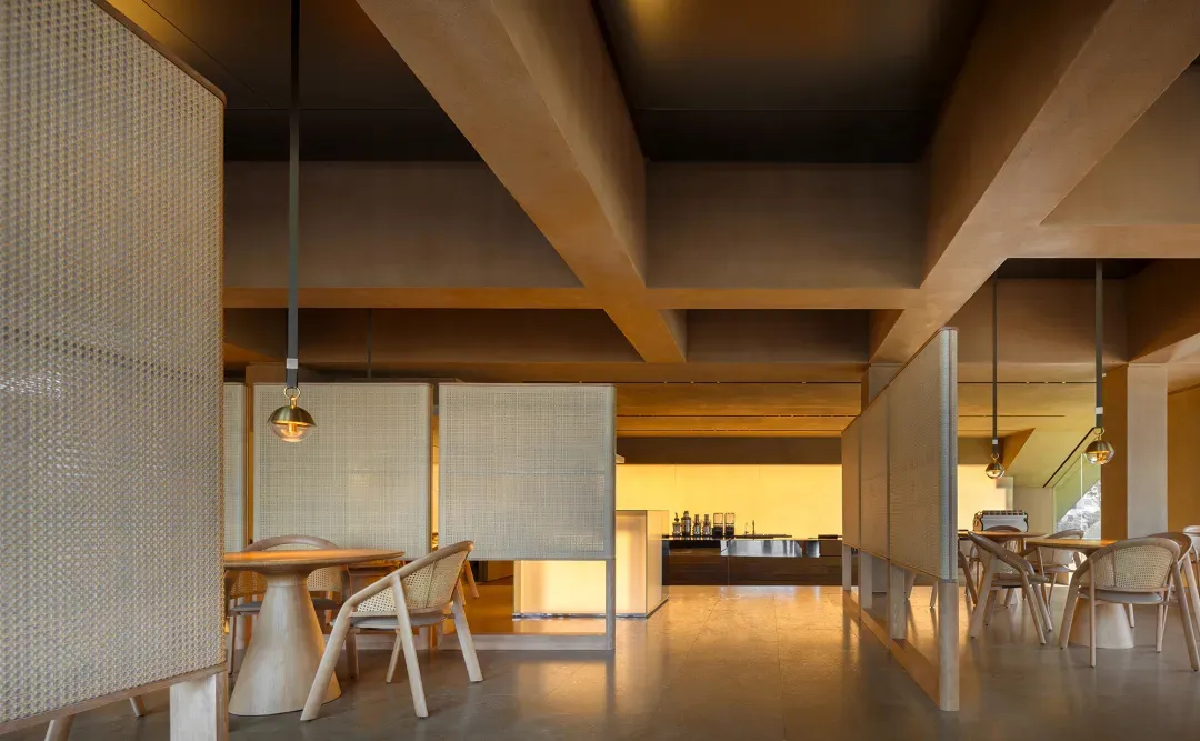 A minimalist restaurant interior with concrete flooring and wicker furniture.