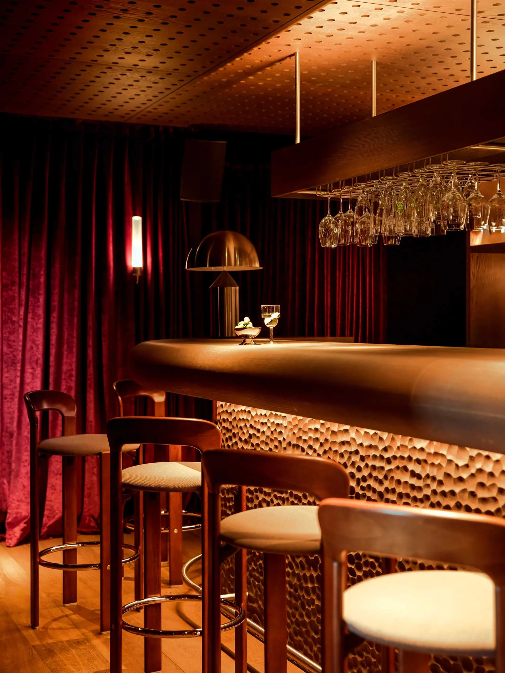 A modern restaurant bar with a wooden counter featuring lit up stools and hanging glasses.