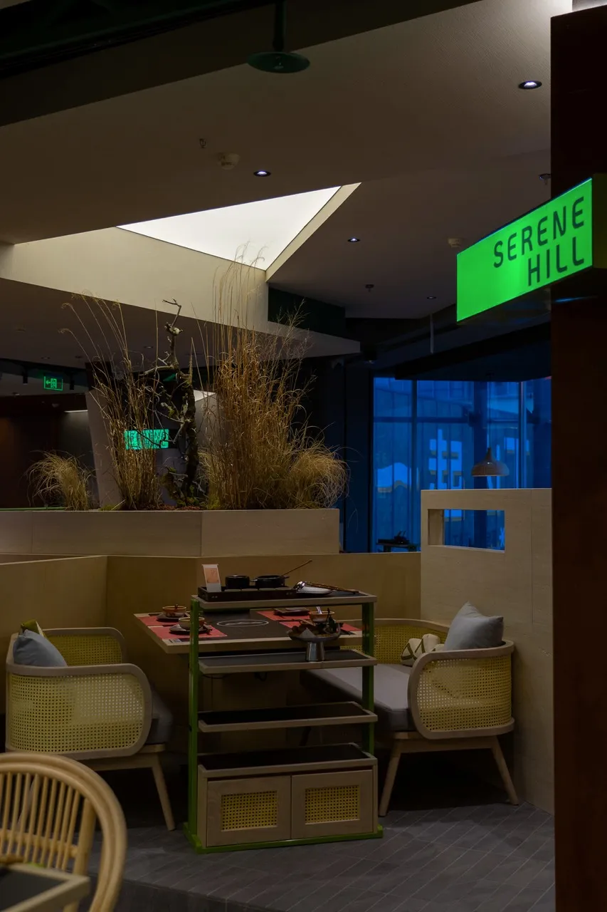 Modern cafe interior featuring wooden furniture, potted plants, and a green sign reading 'Serenity Hill'.