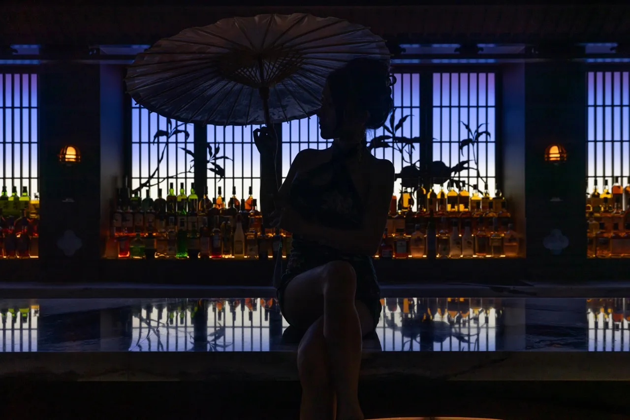 Modern cocktail bar with glass walls and bottles in the background.