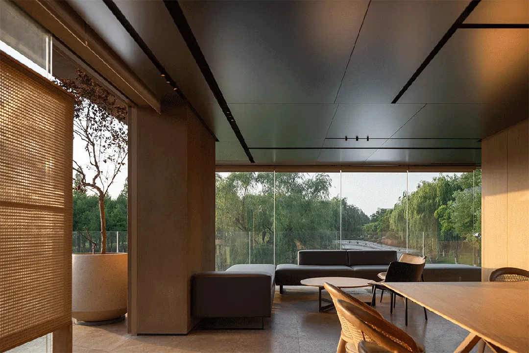 A modern minimalist living room with concrete walls and floor, framed by a large glass window overlooking a serene outdoor la