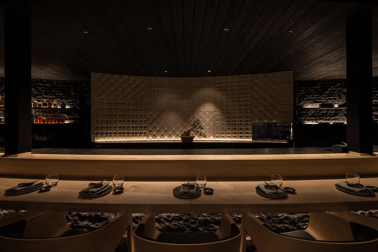 A modern restaurant interior with wooden tables and light-textured stone walls.