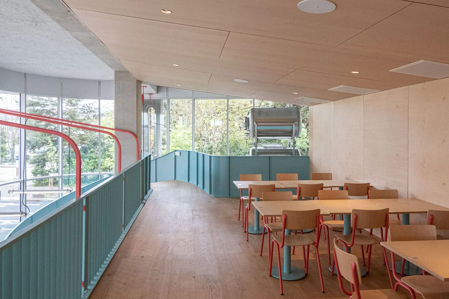 工業風主題的餐廳室內,搭配木製餐桌椅、大型窗戶與窗外綠意。