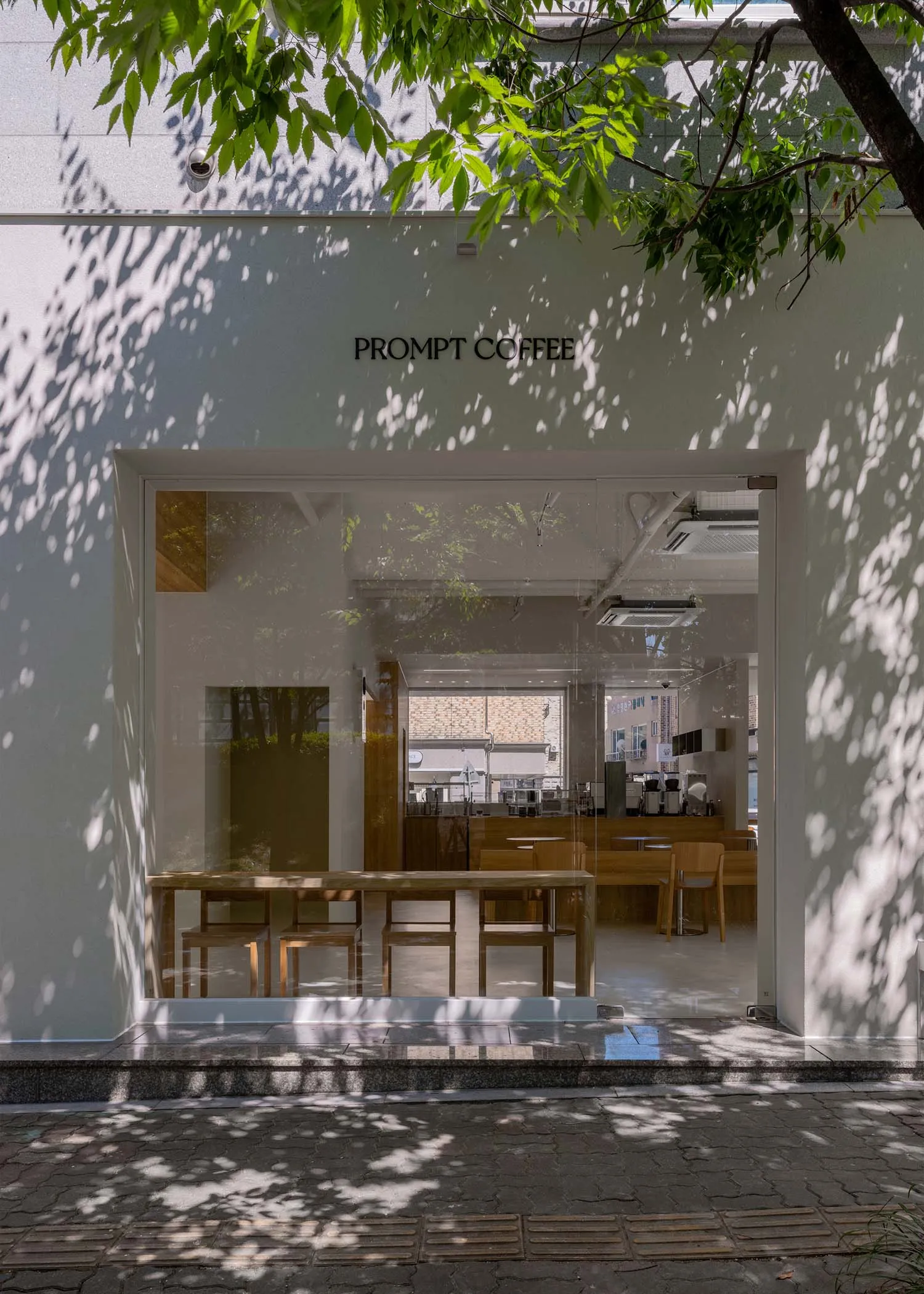 A minimalist coffee shop with glass and wooden features, seen from the exterior.