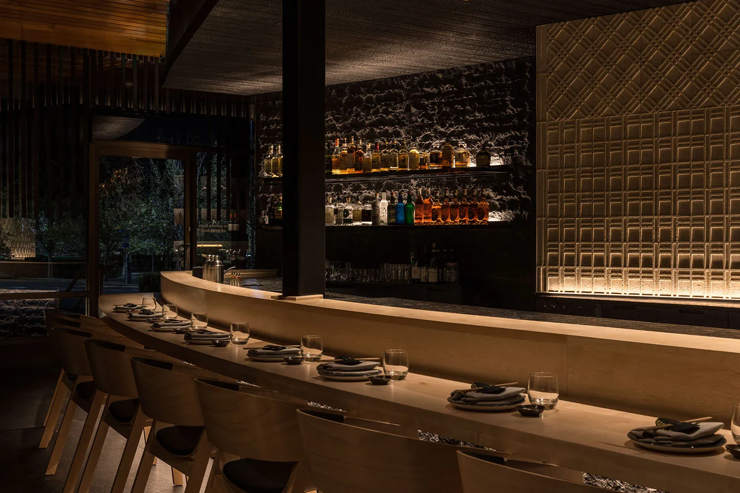 A minimalist restaurant bar interior with wooden seating and stone counter.