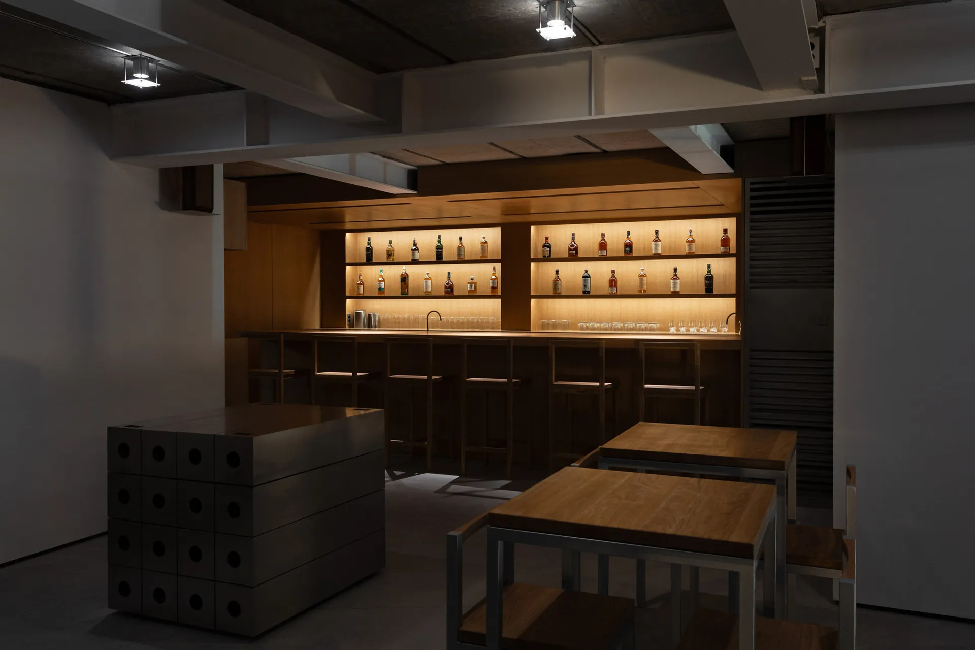 A modern bar counter with wooden surfaces and illuminated shelves showcasing various bottles of liquor.