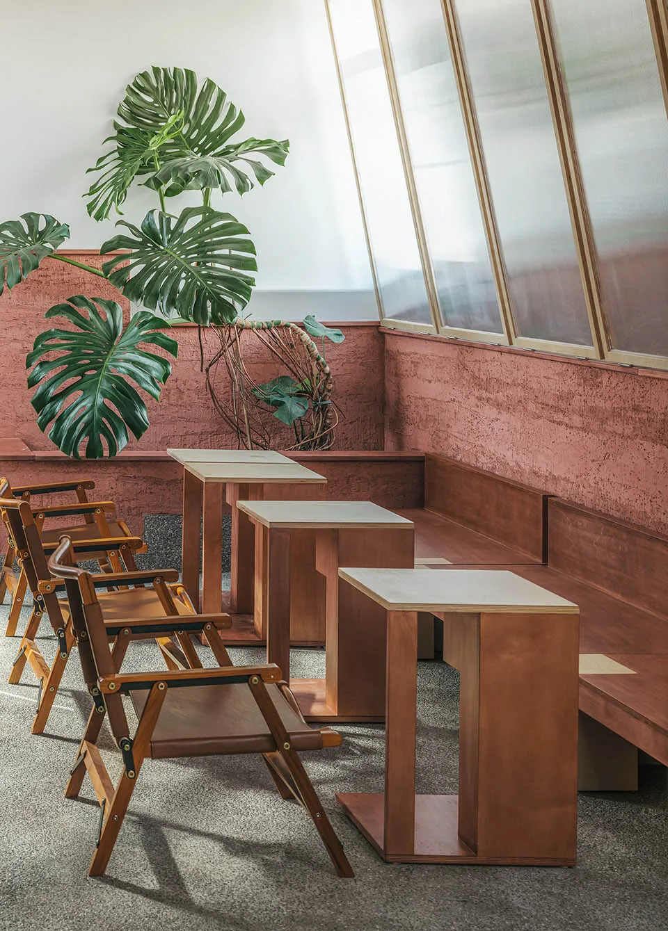 A modern cafe interior featuring wooden furniture, concrete seating, and large glass windows.