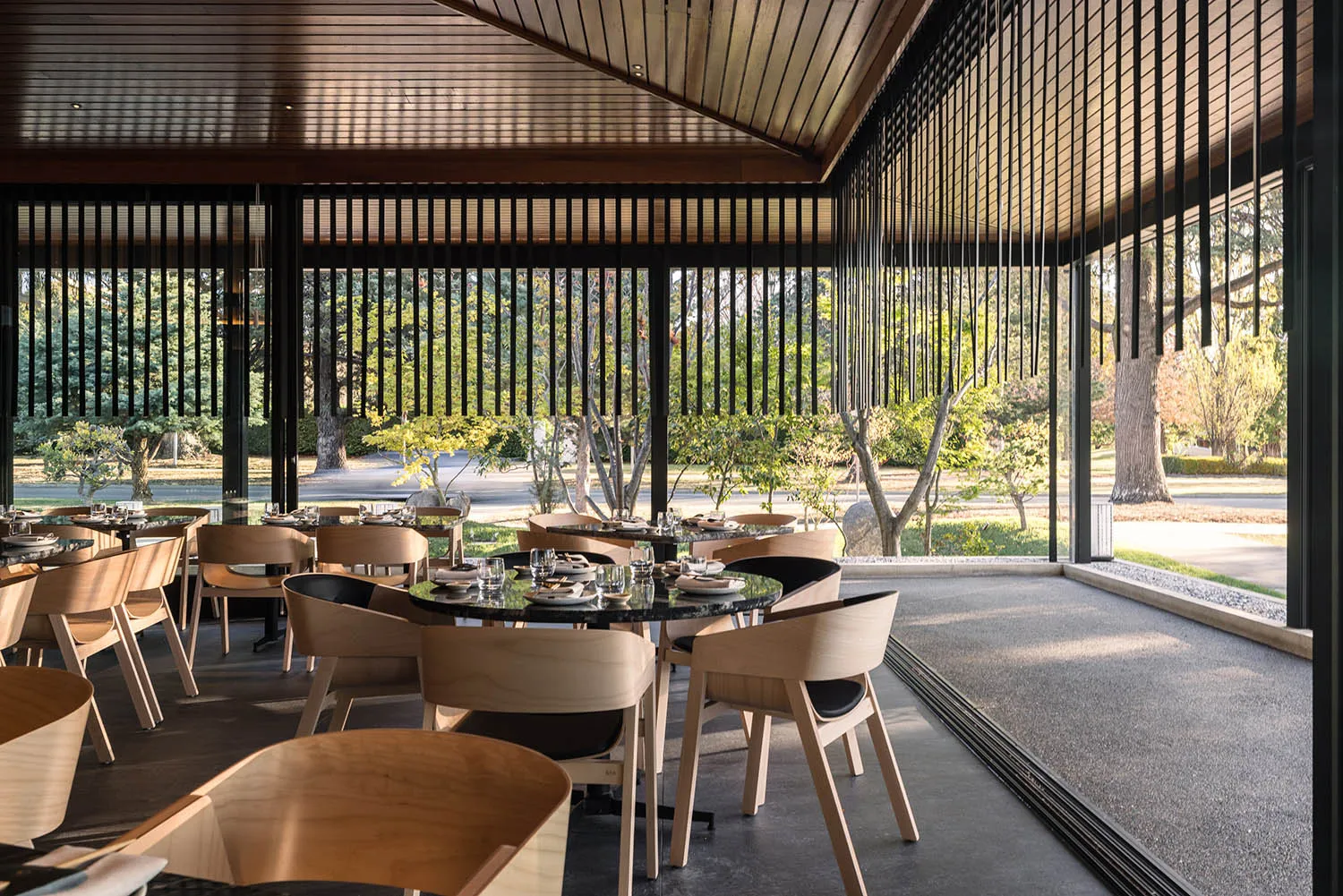 現代餐廳室內,混凝土地板、木質家具,以及可眺望綠意的大窗。