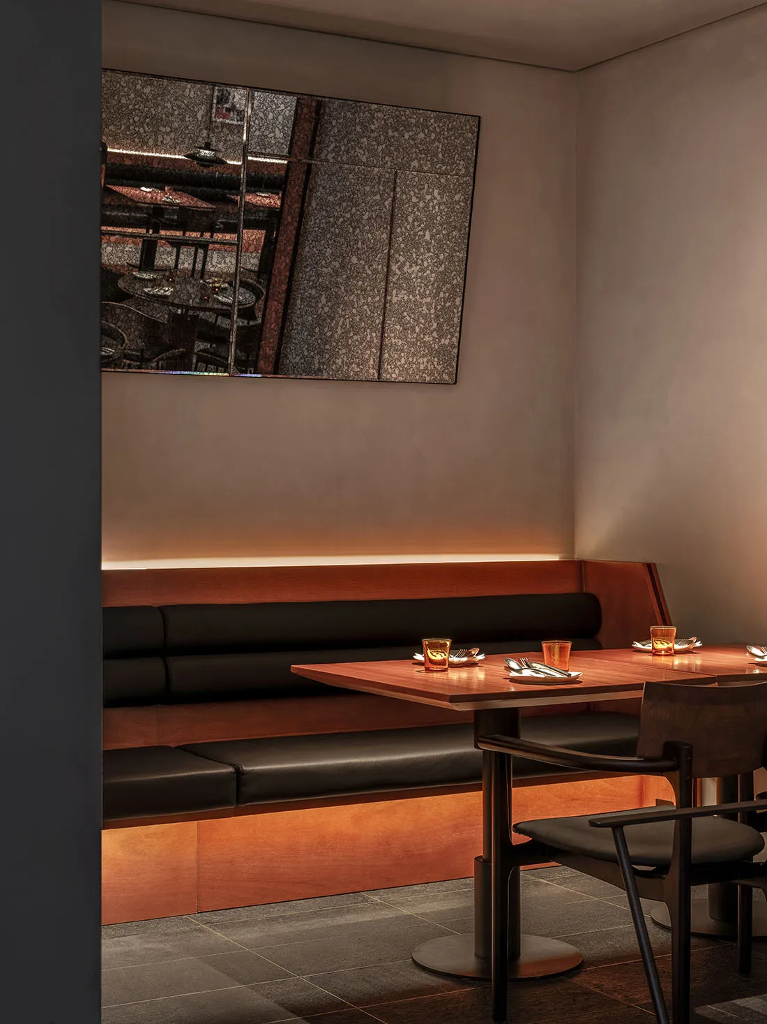 A cozy restaurant dining area with wooden tables and black-leather benches, featuring simple table settings and warm lighting