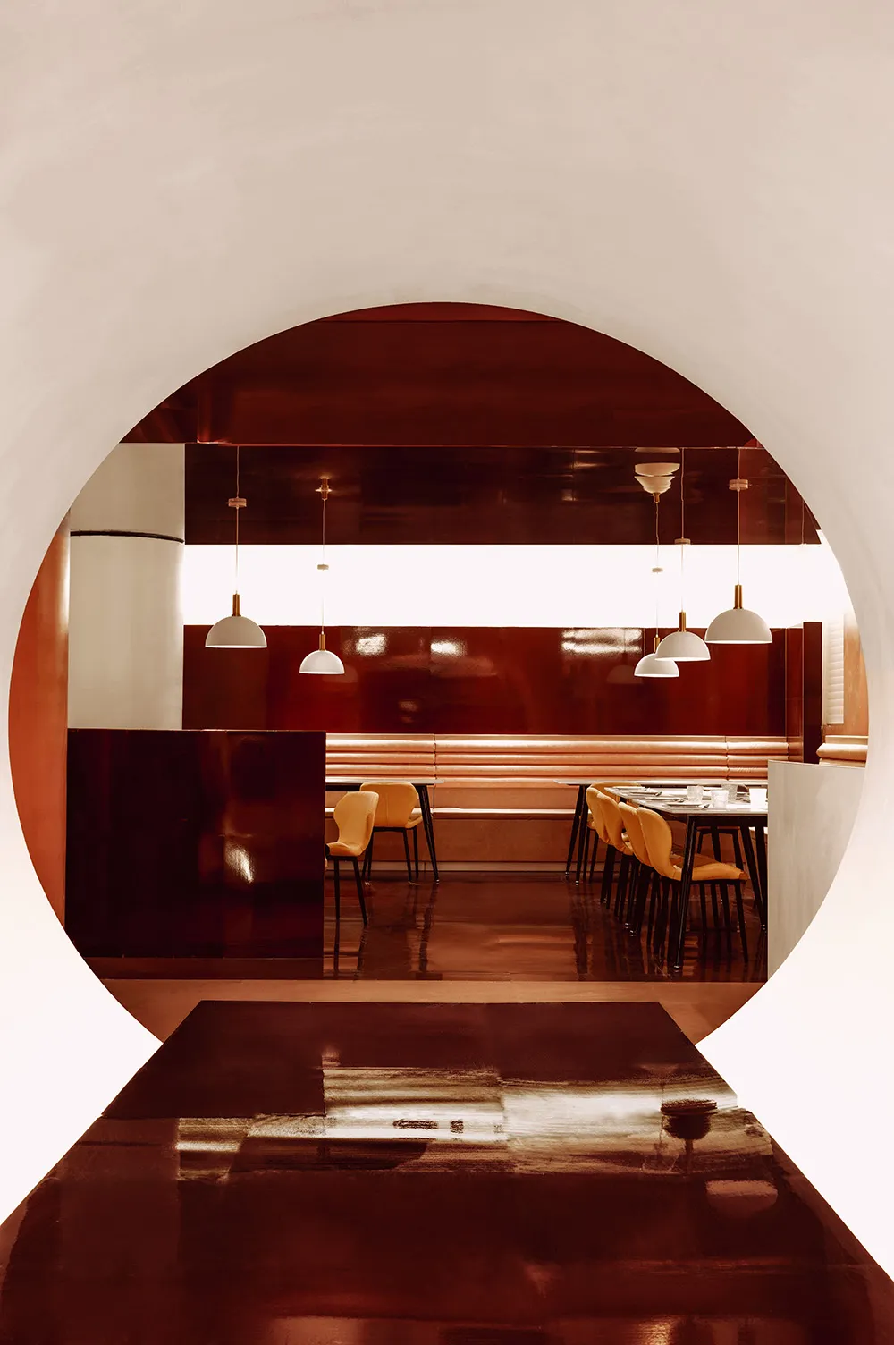 A modern restaurant interior with red metallic walls and white pendant lights.