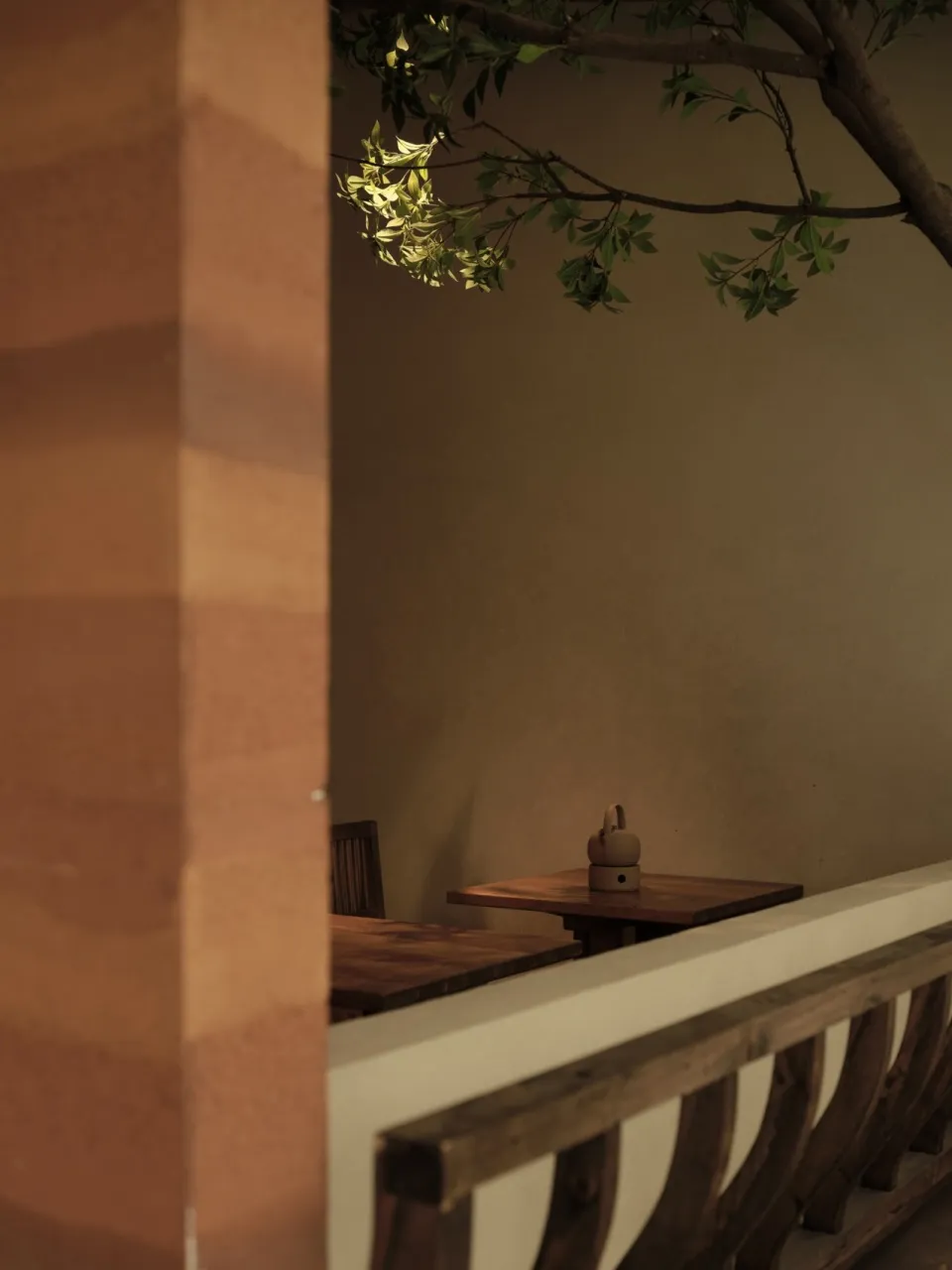 A minimalist restaurant with wooden tables and chairs, featuring a natural tree branch extending from the ceiling.