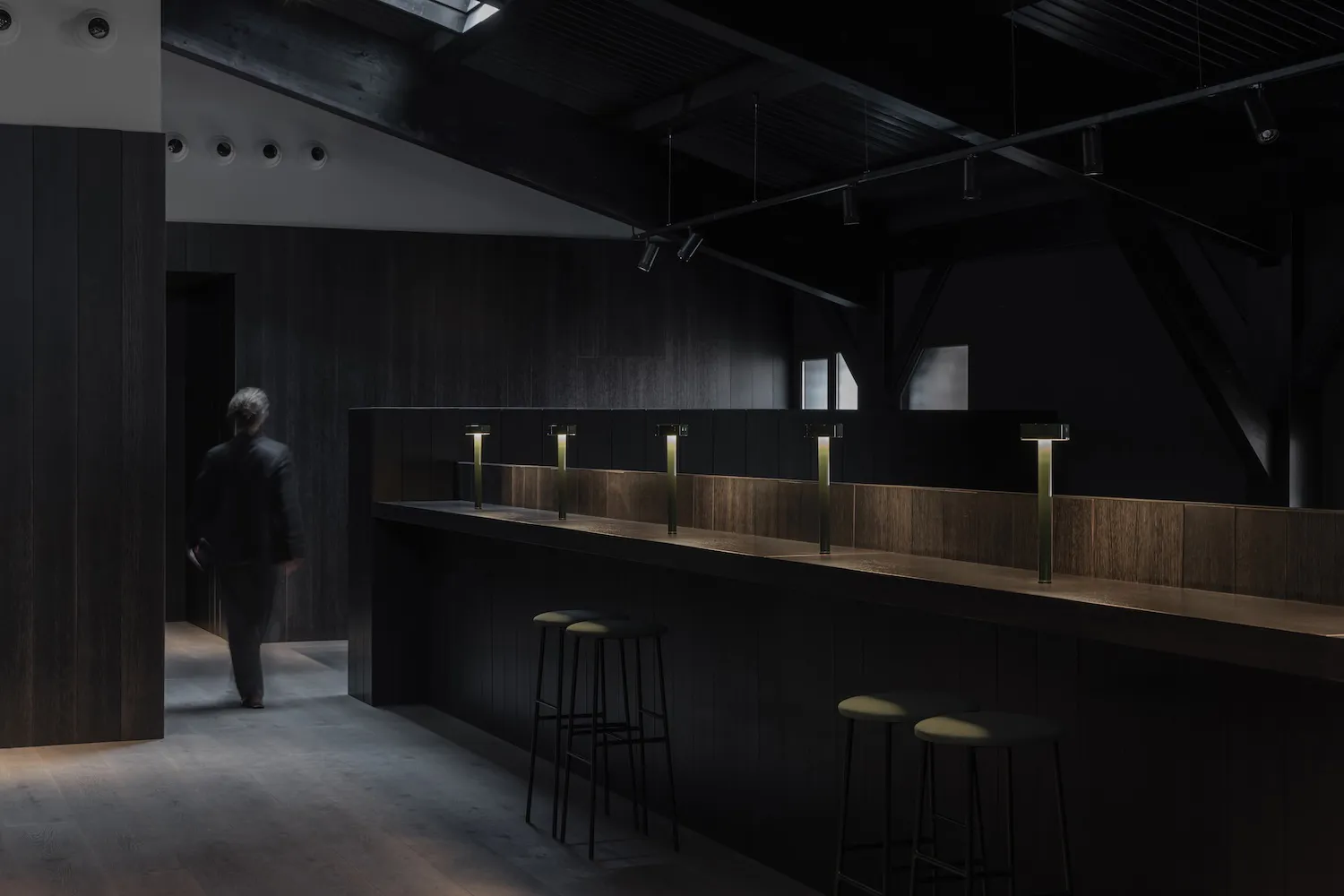 A minimalist bar counter made of modern black wood, featuring sleek lighting fixtures and stools.
