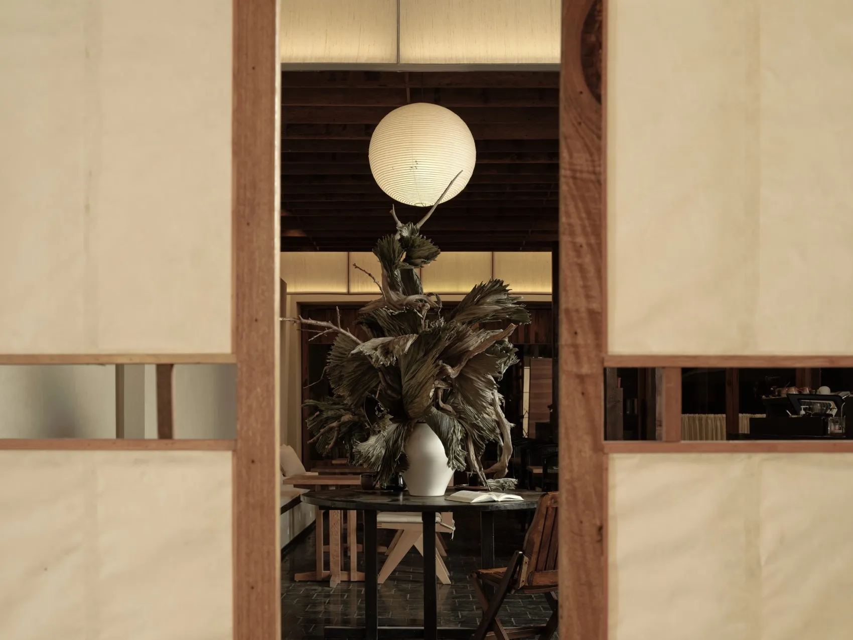 A modern restaurant interior featuring a wooden table with a decorative plant arrangement, and a spherical light fixture hang
