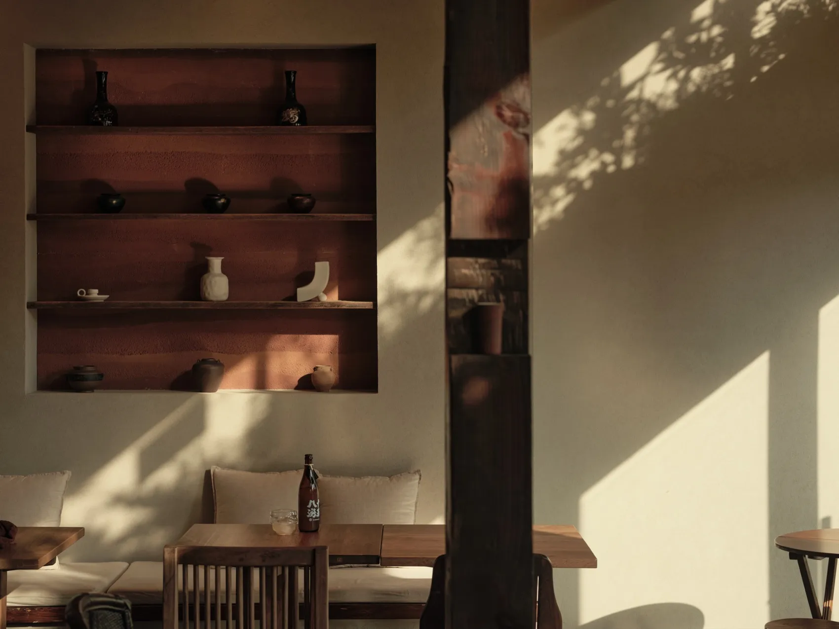 A minimalist cafe interior featuring wooden furniture and shelves.