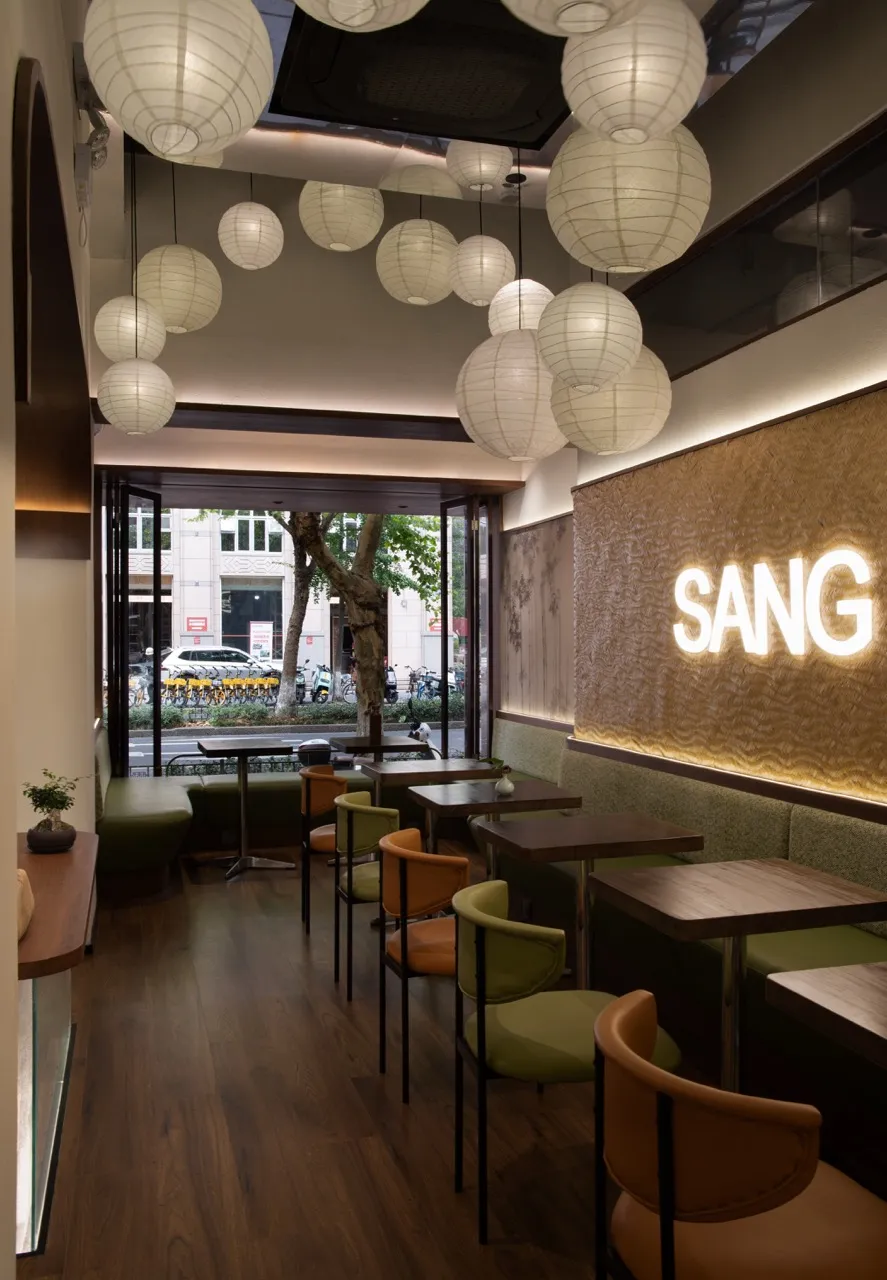 A modern cafe interior with hanging paper lanterns, wooden furniture, and upholstered seating.