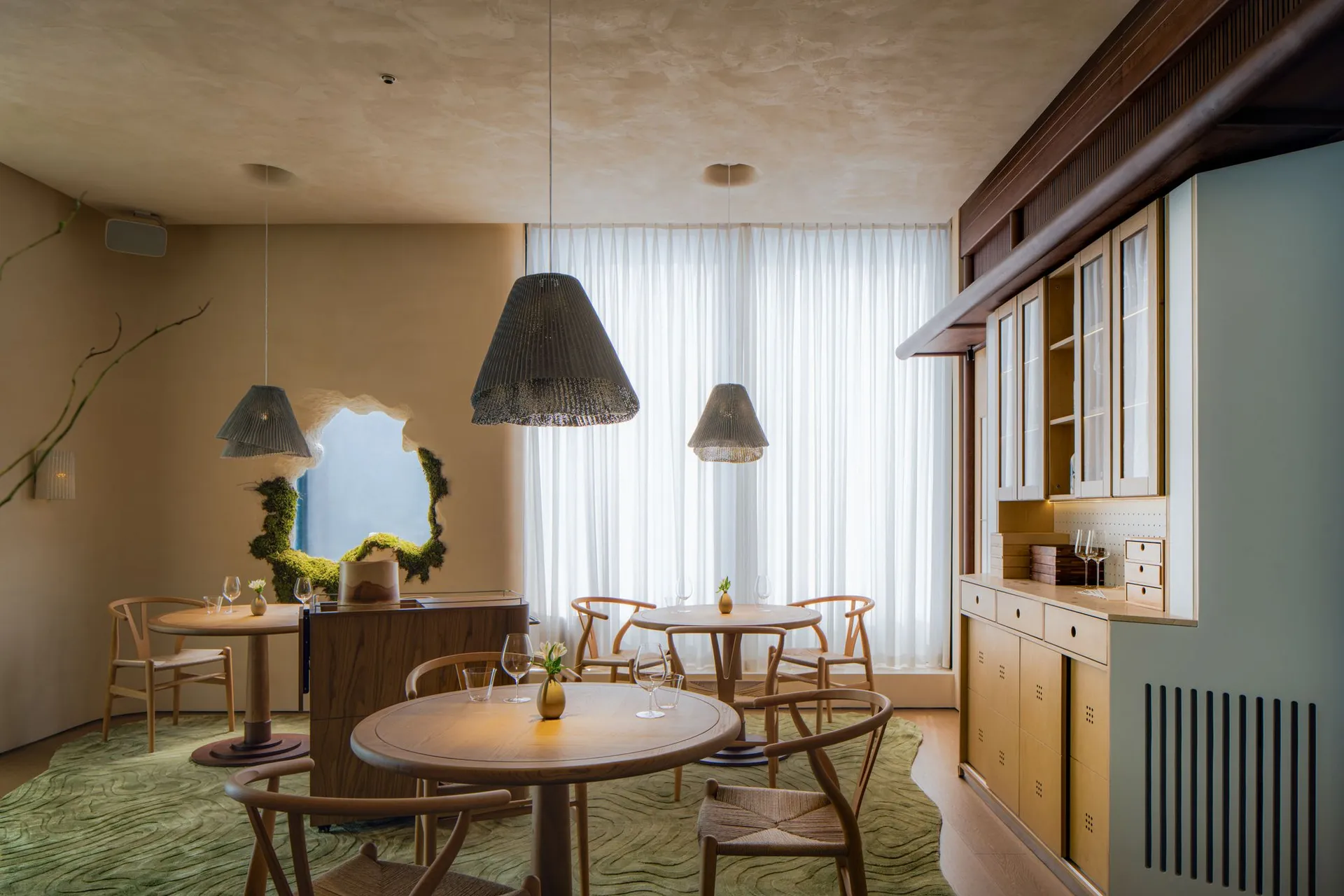 Modern restaurant interior with wooden tables, fabric curtains, and a window showcasing the outdoors.