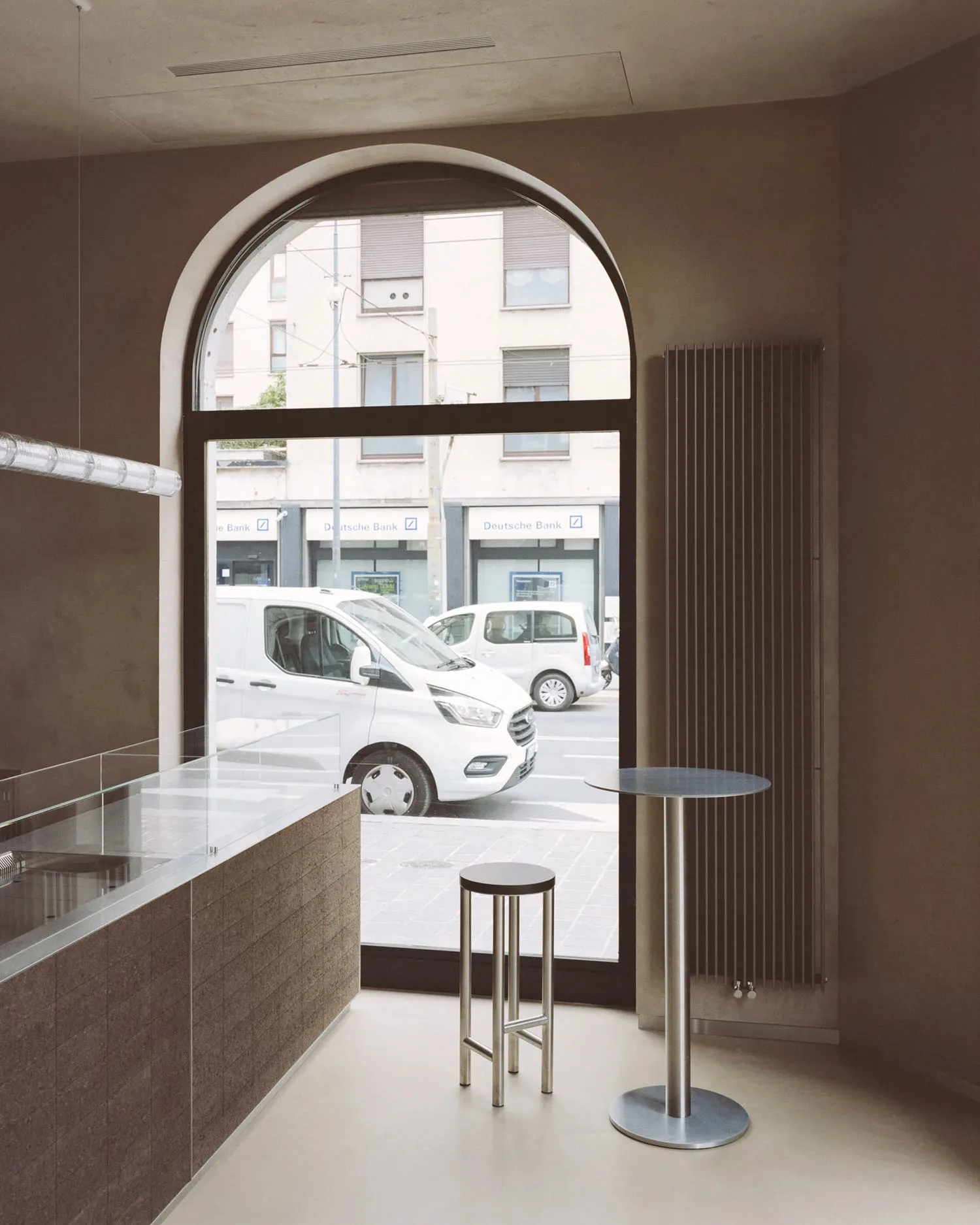 A modern coffee shop with a concrete store counter, high stools, and high table.