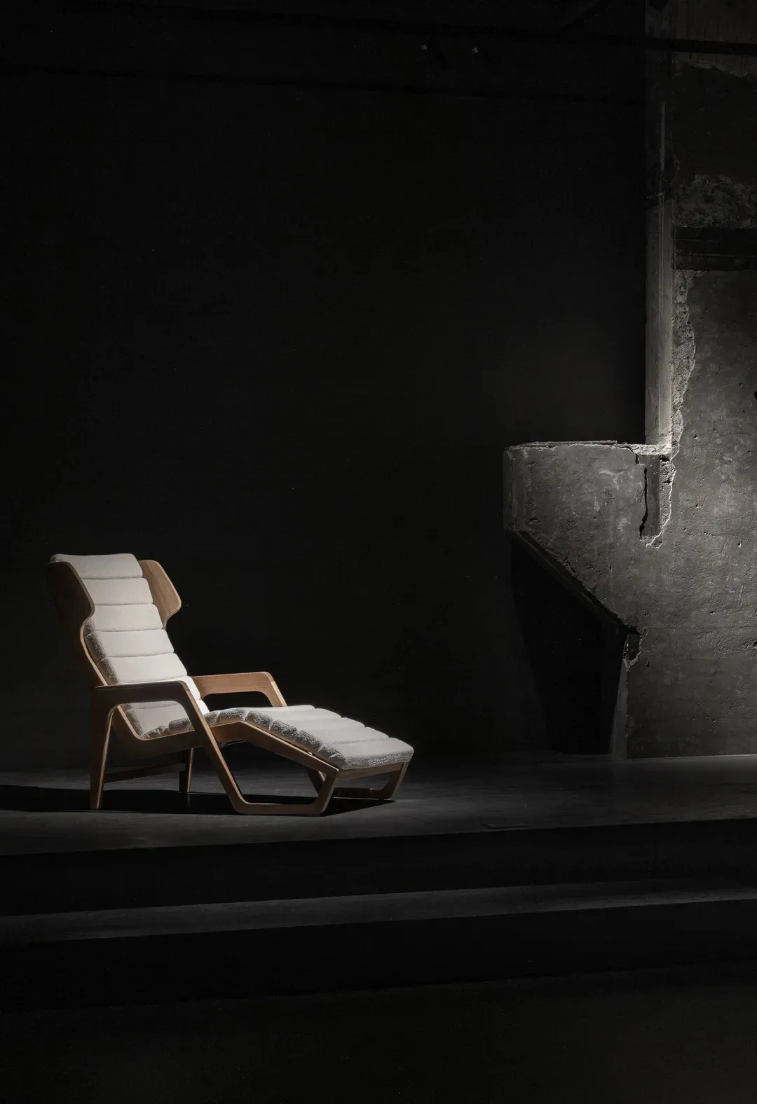 A minimalist chaise lounge with white fabric upholstery in a dark room setting.