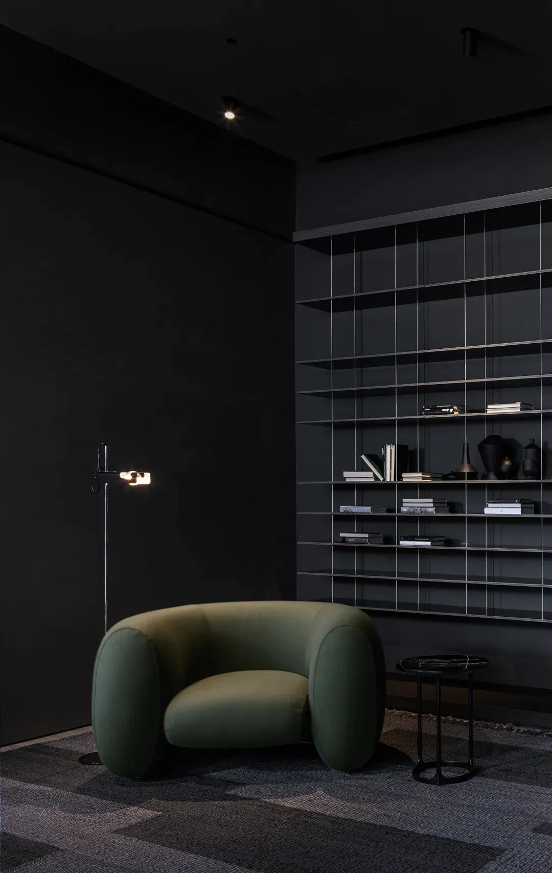 A minimalist modern interior with a green upholstered armchair and black shelving units.