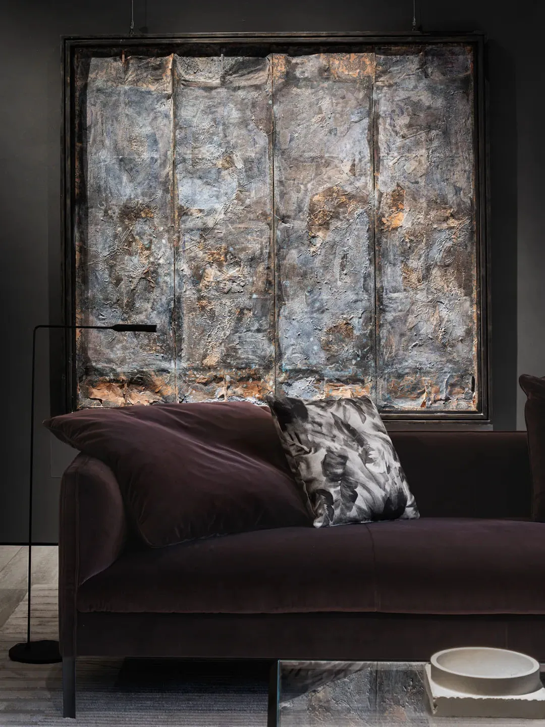 A modern living room featuring a textured metal wall artwork and a comfortable couch with floral-patterned cushions.