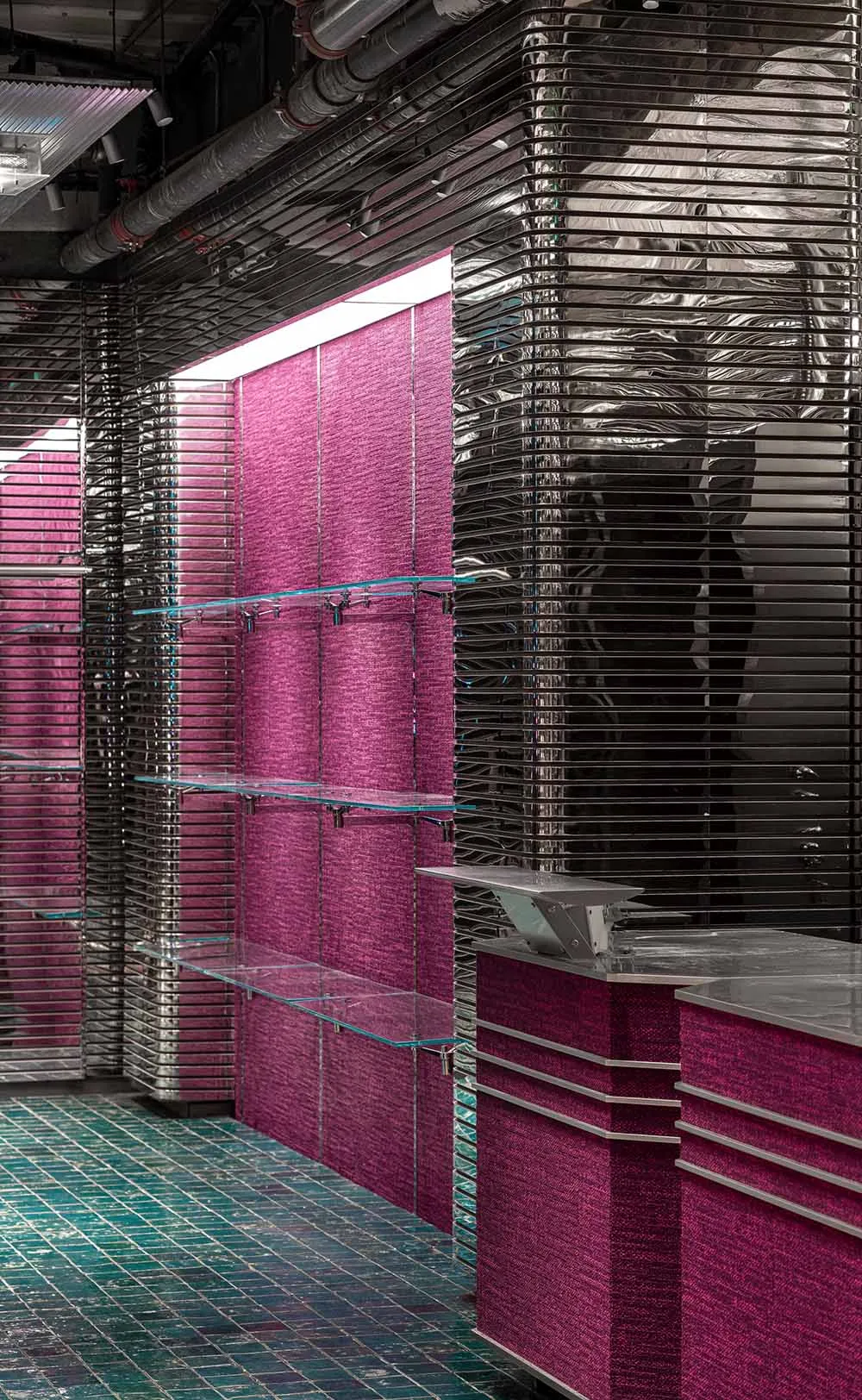 Modern retail space with metallic texture backdrop, glass shelves, and pink textile elements