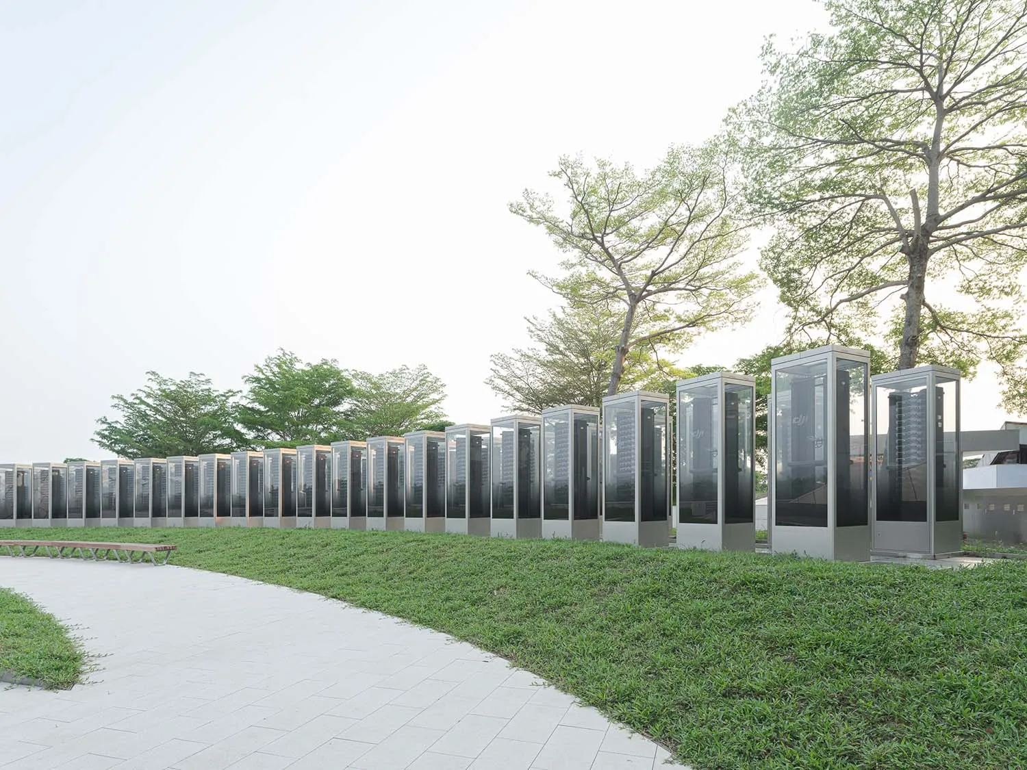 Rows of modern glass and steel structures in a park setting with greenery and trees.