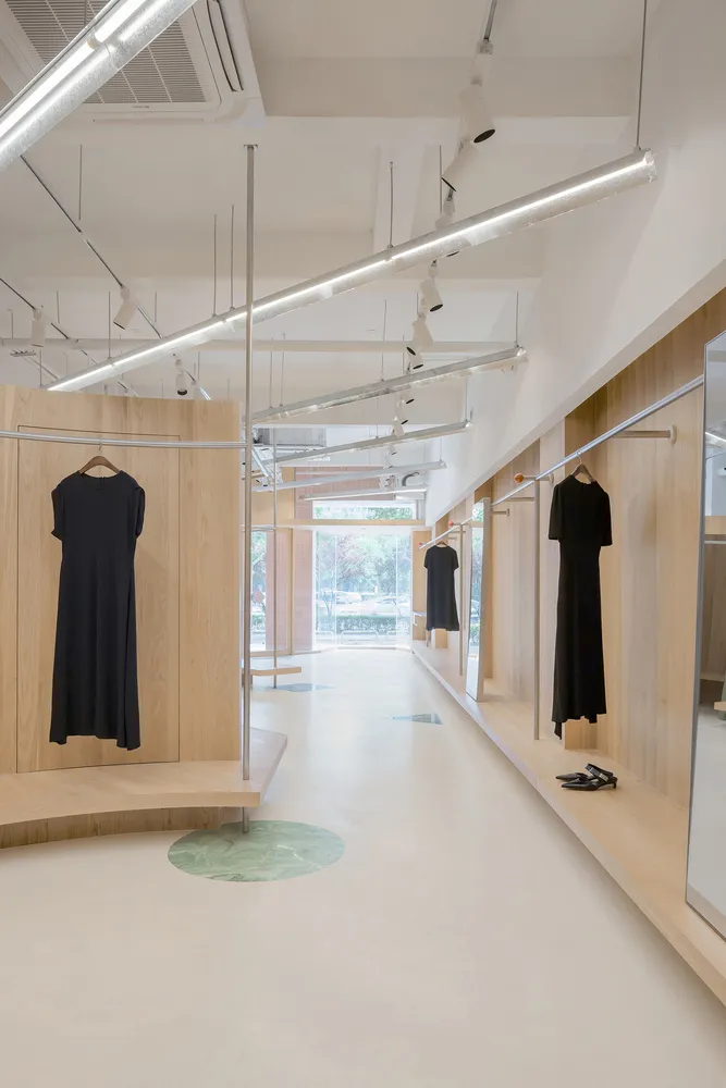 A clothing shop interior featuring minimalist design with wooden walls, glass doors, and concrete floor.