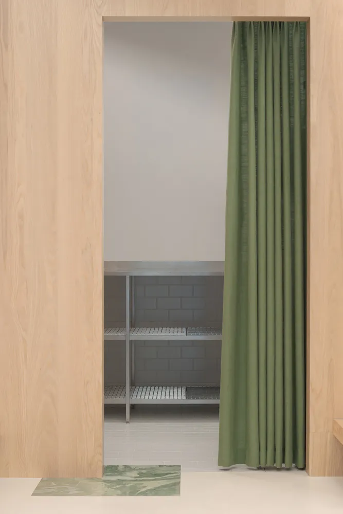 A minimalist kitchen with a green curtain and metallic shelving.