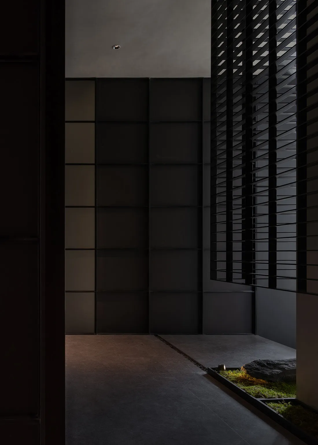 Modern interior corridor with concrete flooring, black glass walls, and black window shutters.