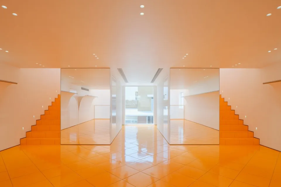 Modern interior design featuring shiny yellow tiled floor, concrete walls, and mirrored surfaces.