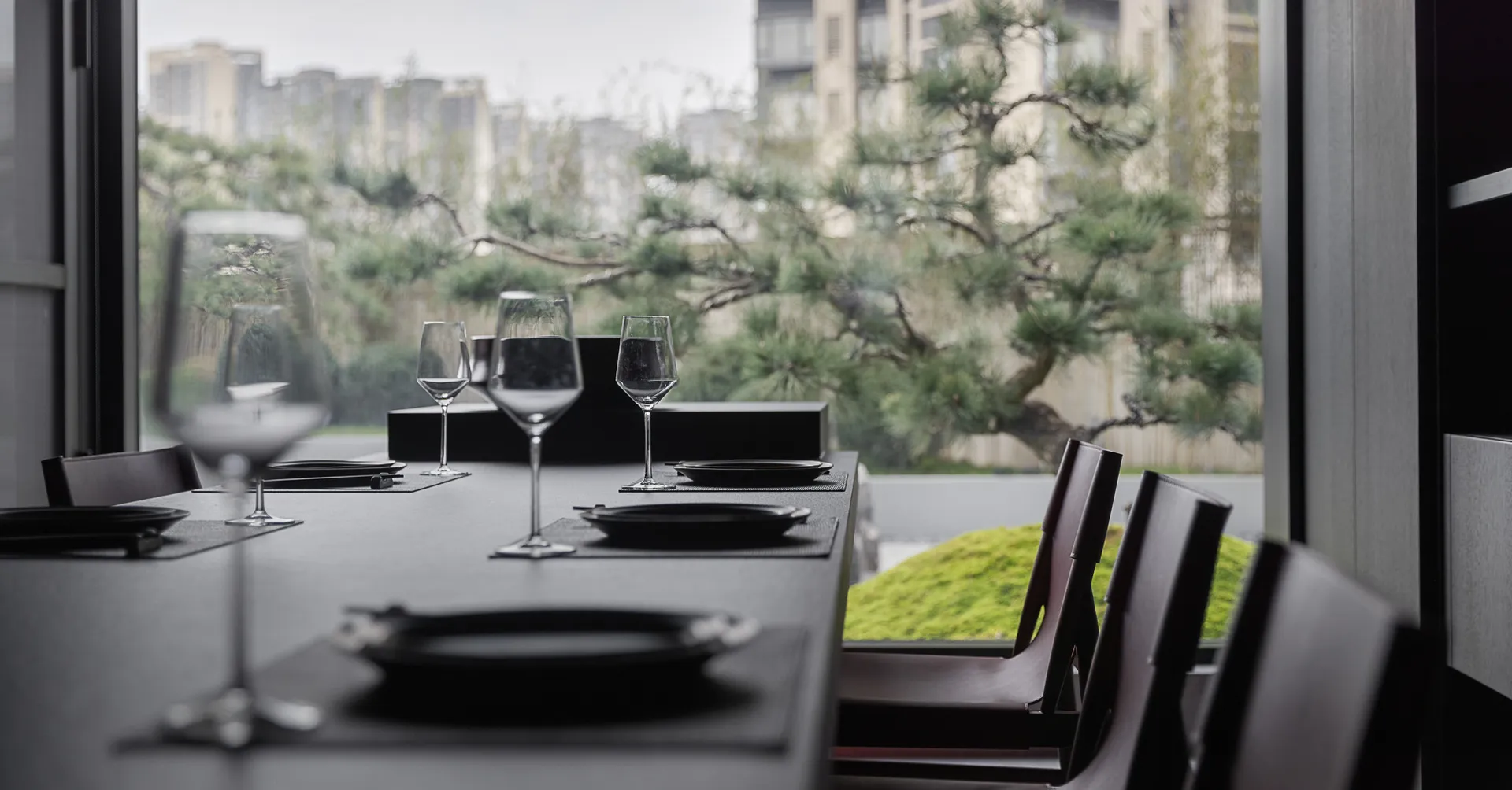 A minimalist dining room with glass dinnerware, set on a sleek, dark table with modern chairs.