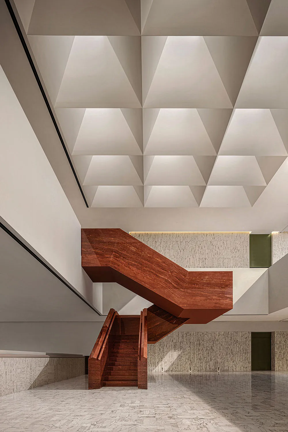 Modern building interior featuring a wooden staircase with geometric ceiling panels.