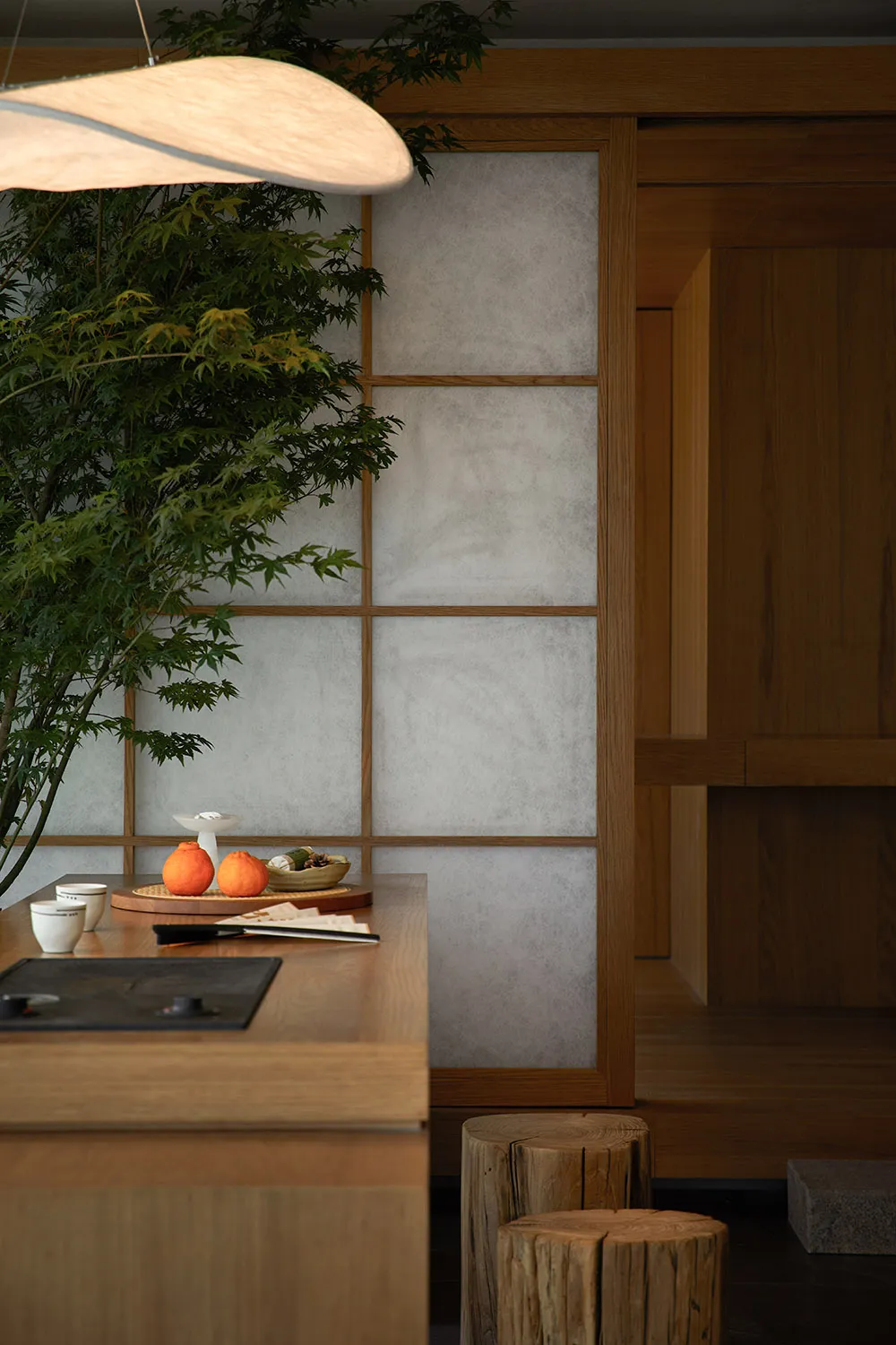 A minimalist kitchen with paper walls and wooden cabinets features an orange fruit on a plate and a modern light fixture.