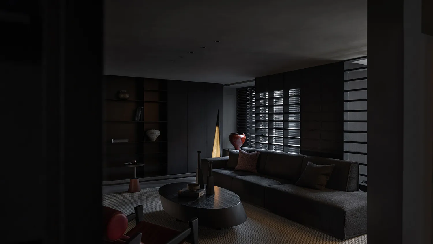 A minimalist living room with dark, sleek black furniture, a rug, and a light lamp.