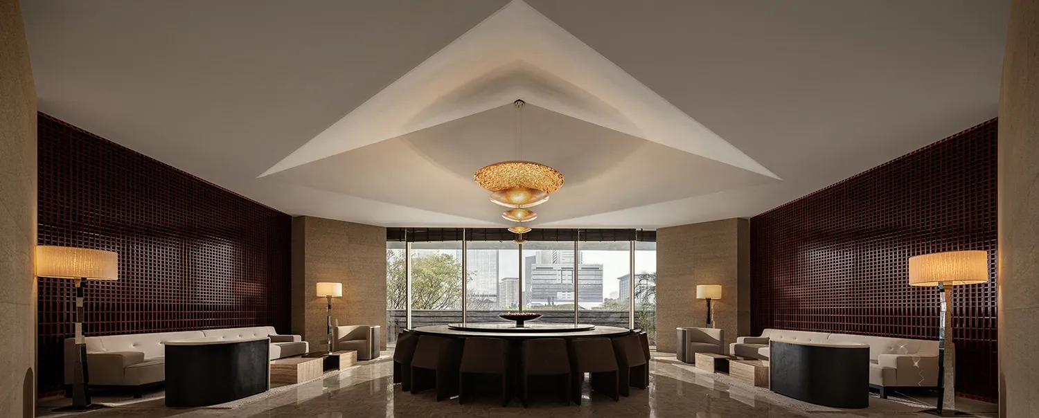 A modern hotel lobby features marble and concrete materials with a central dining table and seating areas.