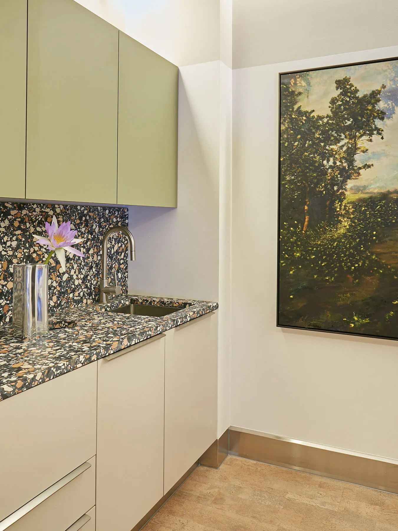 A minimalistic kitchen featuring a terrazzo countertop with a single purple flower in a vase.
