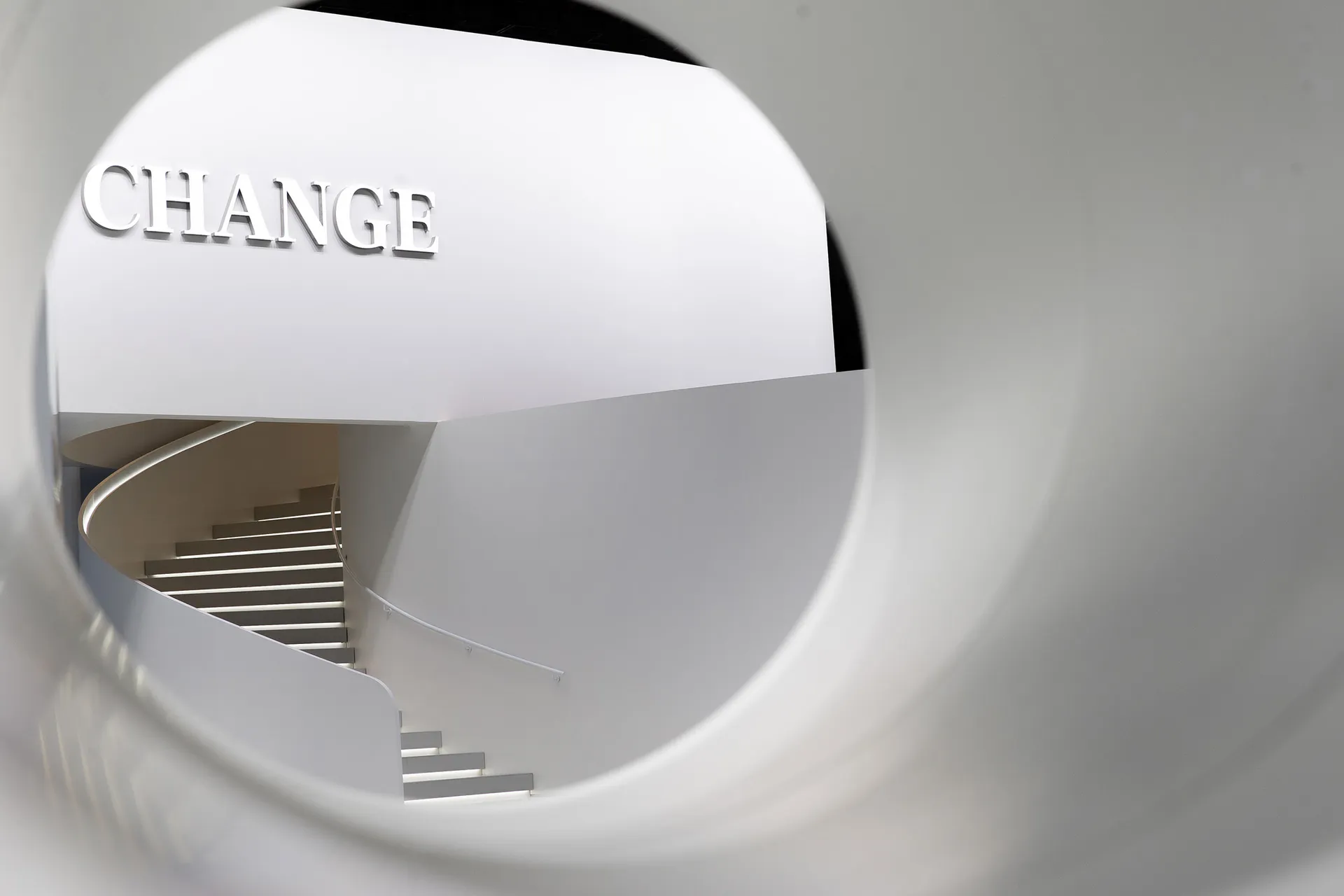 A minimalist staircase with white walls and steps, viewed through a circular opening.