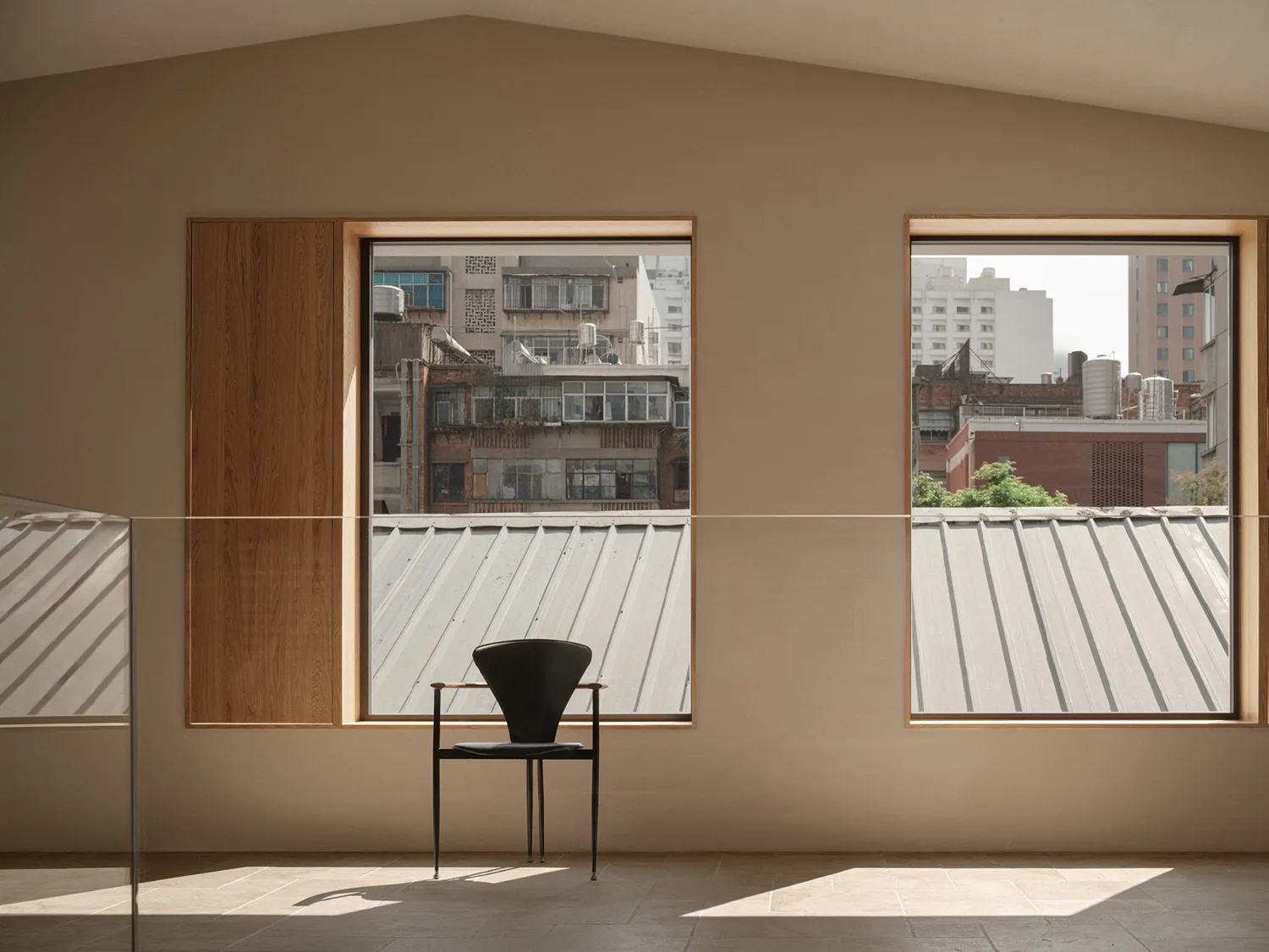 A minimalist black chair sits in front of a large window overlooking the cityscape of a modern urban area.