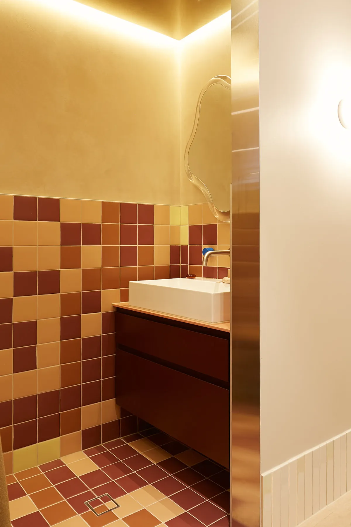 A modern bathroom with ceramic tiles on the walls and floor, featuring a sink and a sleek vanity unit.