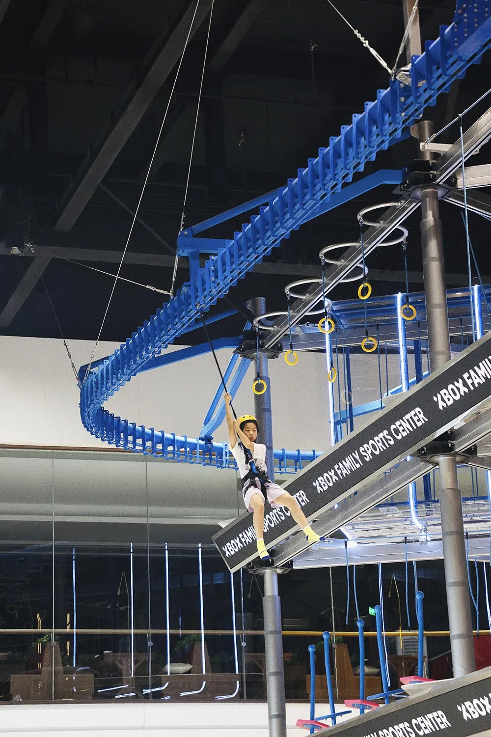 A child is climbing on an industrial-style playground rope course comprised of metal structures and rings.