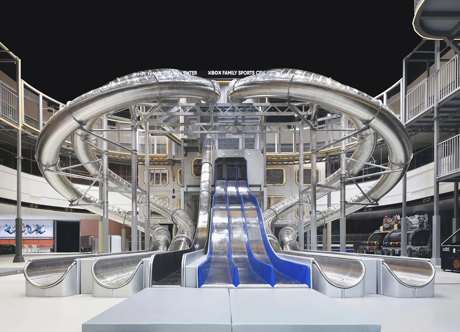 A large, indoor playground featuring a metal spiral slide and a series of tubes connected by a central structure.