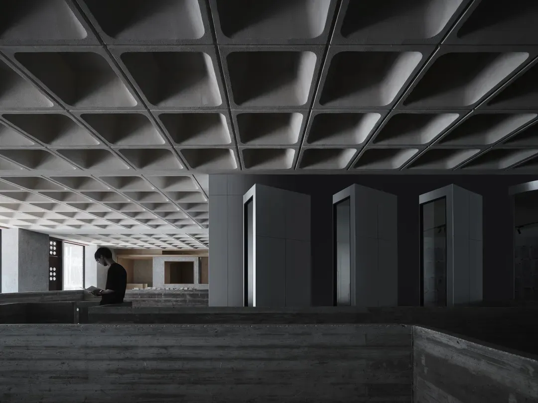 A minimalist office interior featuring concrete walls and a textured ceiling panel.