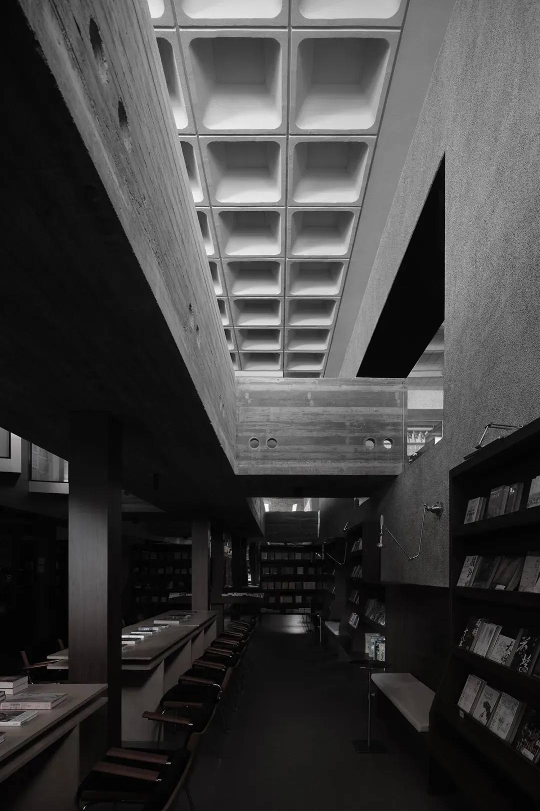 A black and white photograph of a modern library interior with concrete walls and a grid ceiling.