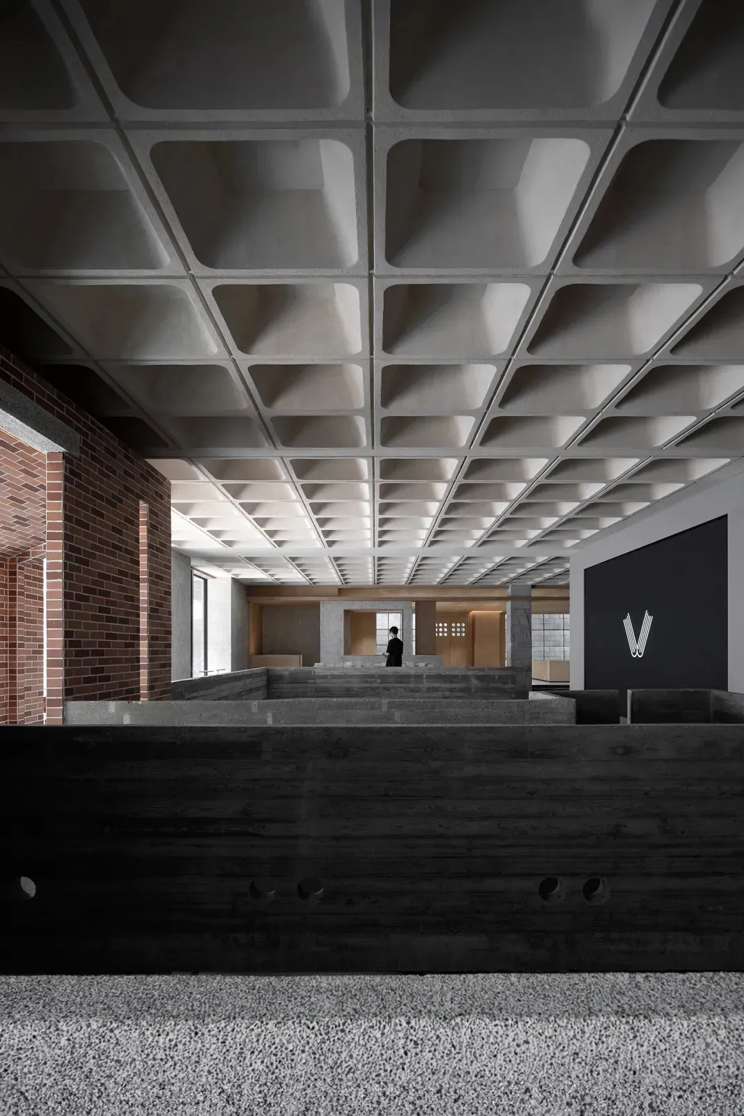 A modern lobby with a concrete ceiling and floors, featuring geometric shapes and a minimalist design.