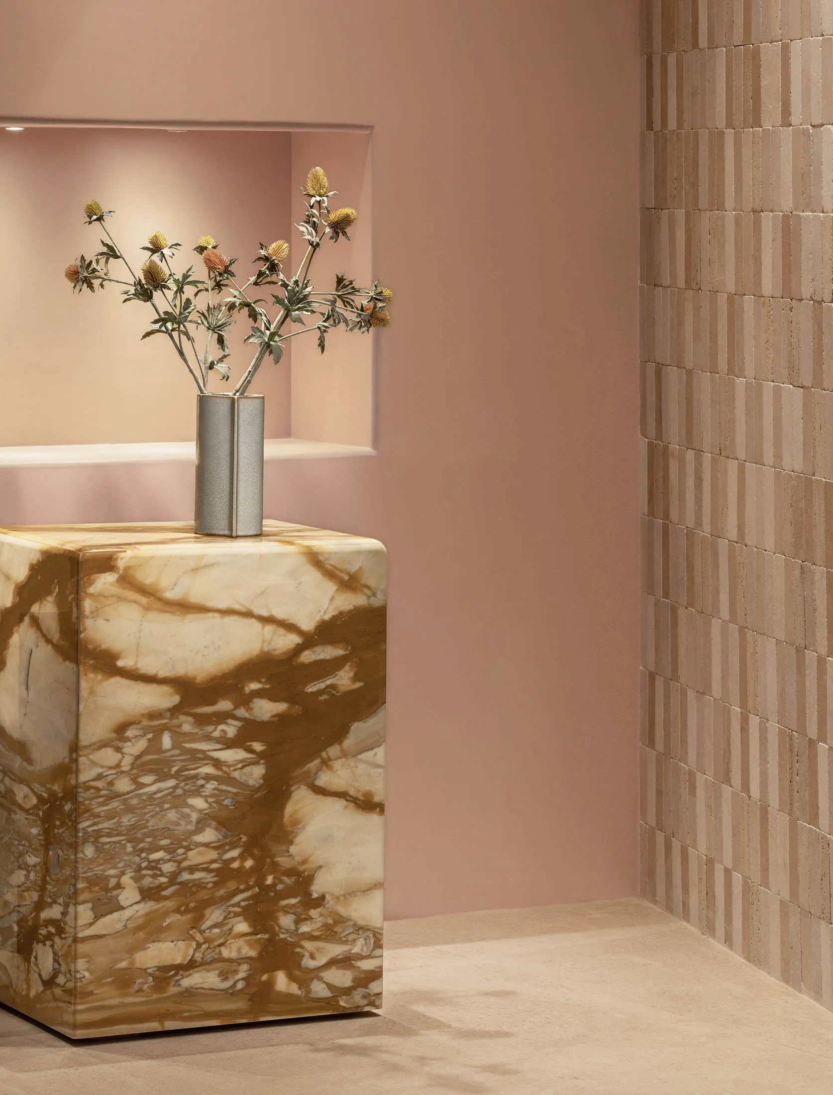 A modern marble table featuring a vase of flowers in a silver vase against a pink wall and beige tiled floor.